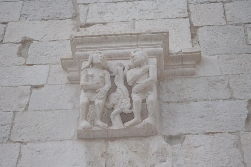 Mensola scolpita con Adamo ed Eva ai lati dell'albero con il serpente, murata in una parete in conci di pietra