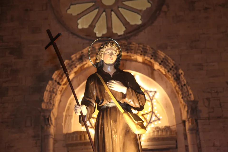 La statua di San Nicola Pellegrino con aureola e lunga croce, illuminata all'interno di un portale ad arco sormontato da un rosone