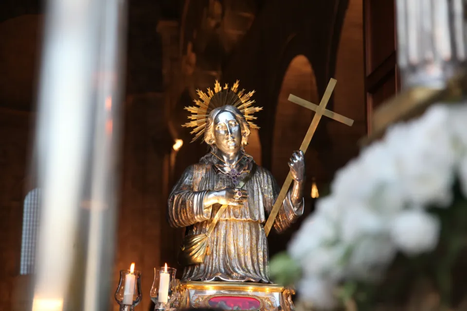 Statua in argento di San Nicola Pellegrino con aureola e croce, ornata di fiori bianchi, all'interno di una chiesa prima dell'uscita in processione