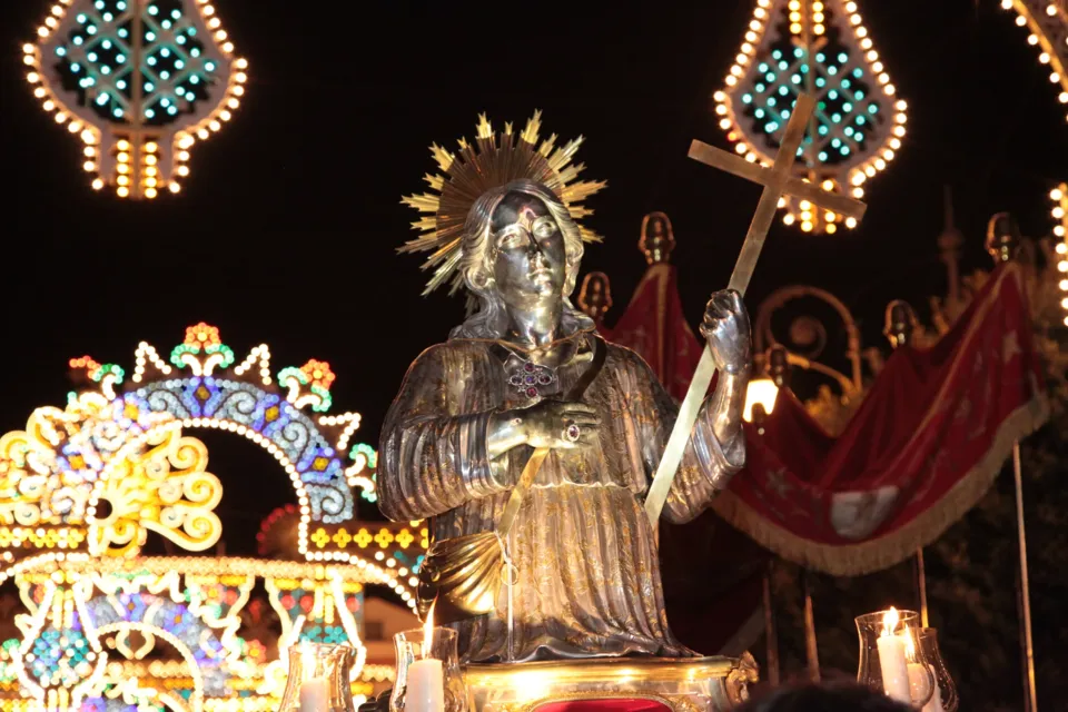 La statua d'argento di San Nicola Pellegrino con raggiera e croce, tra le luminarie colorate della festa, di notte