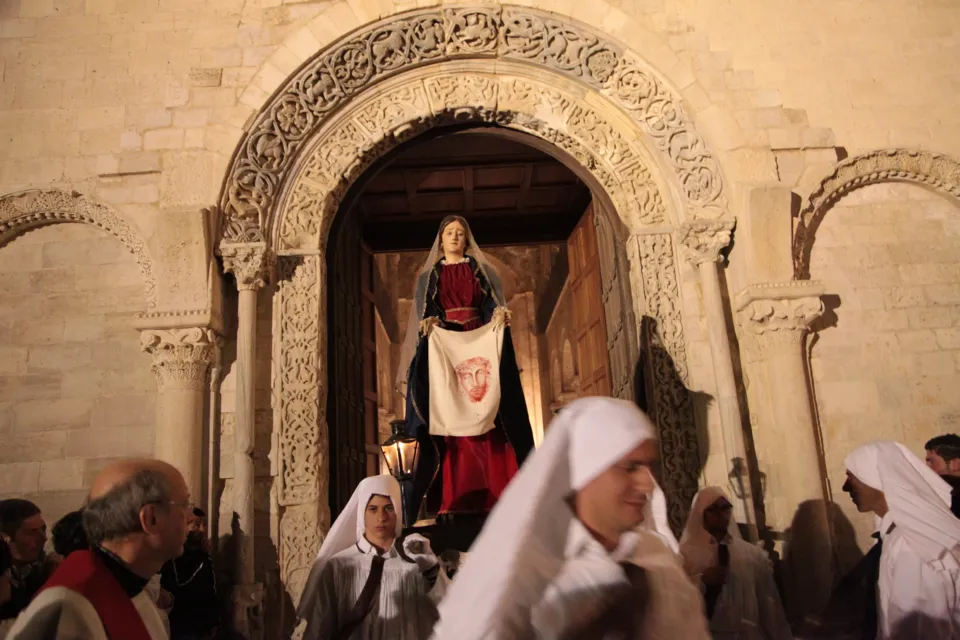La statua della Veronica che mostra il velo con il volto di Cristo esce dal portale romanico tra confratelli incappucciati