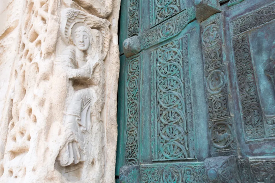 Dettaglio dello stipite in pietra scolpita con una figura e della porta in bronzo con formelle decorate del portale della Cattedrale