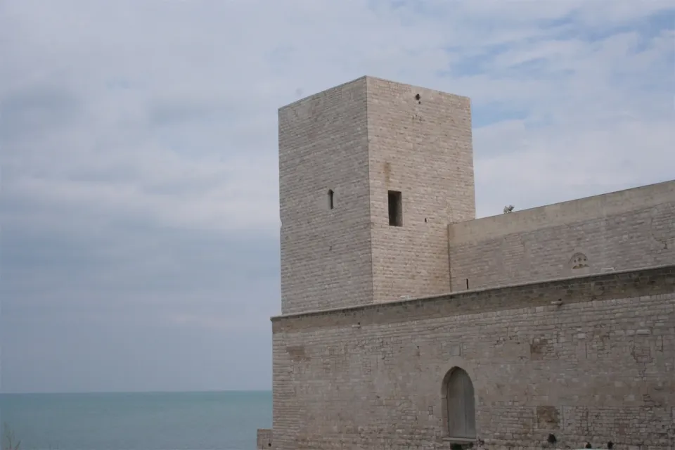 Torre quadrata e cortina muraria del Castello Svevo con il mare sullo sfondo, sotto un cielo grigio