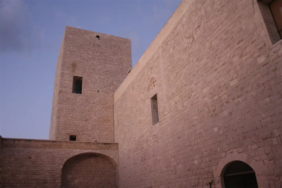 Una delle torri quadrate del Castello Svevo vista dal cortile, in conci di pietra chiara, con cielo blu serale