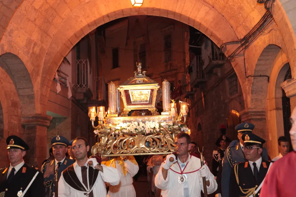 L'urna argentea delle reliquie di San Nicola Pellegrino portata in processione di notte sotto un grande arco in pietra, scortata da militari e confratelli
