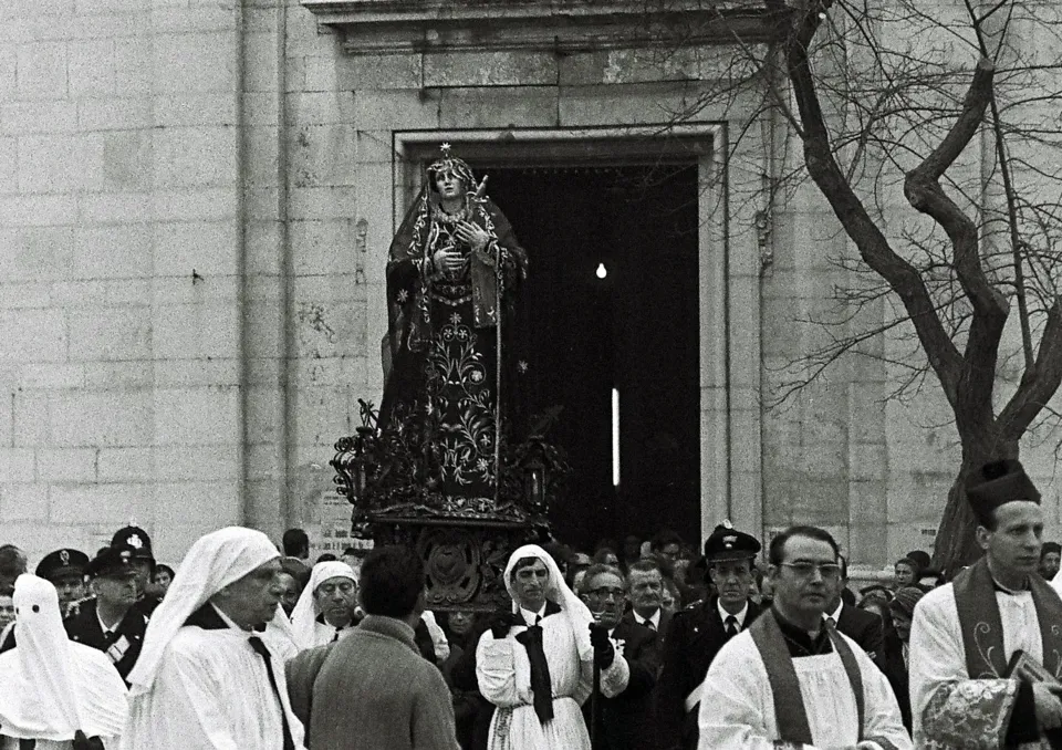 La statua dell'Addolorata esce dal portale di una chiesa, accompagnata da confratelli in bianco, sacerdoti con stola e carabinieri in alta uniforme